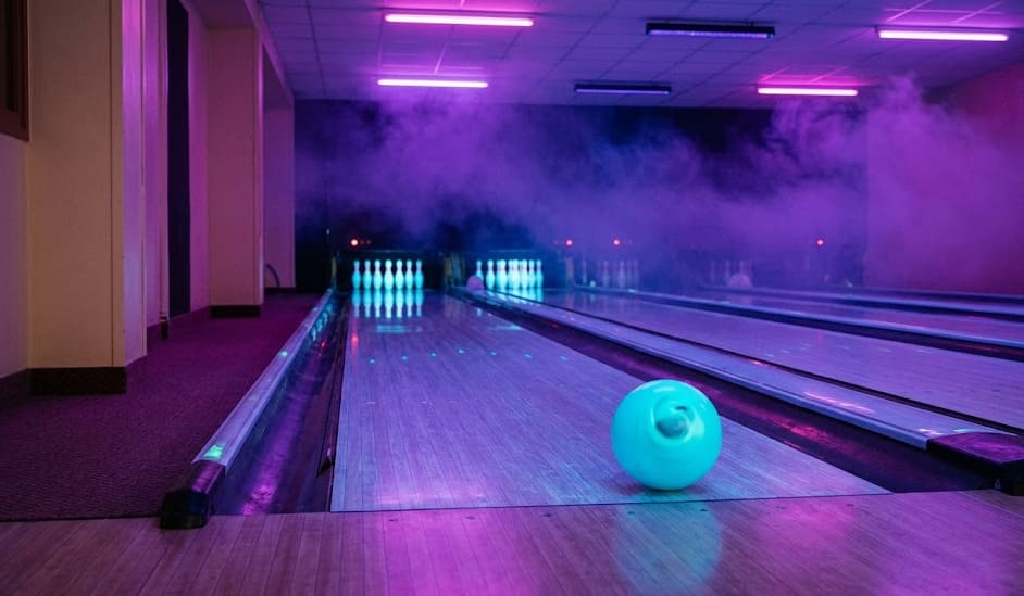 Salle de bowling en cosmic bowling — perspective basse, néons UV, piste vue rasante