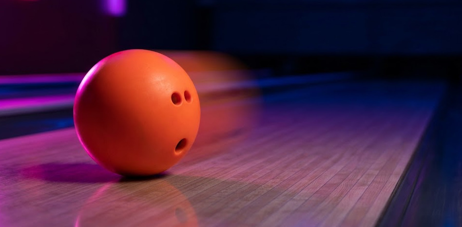 Boule de bowling plastique uréthane orange en mouvement sur la piste, vue rasante avec léger motion blur — l'outil dédié des spares de coin