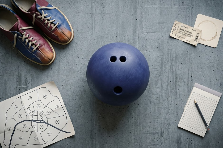 Flat lay éditorial : boule de bowling, chaussures de location et ticket métro RATP sur fond ardoise — sortie bowling à Paris